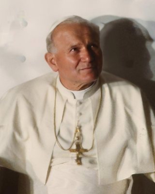 Pope John Paul II in white papal robes and pectoral cross, looking upward with a slight smile